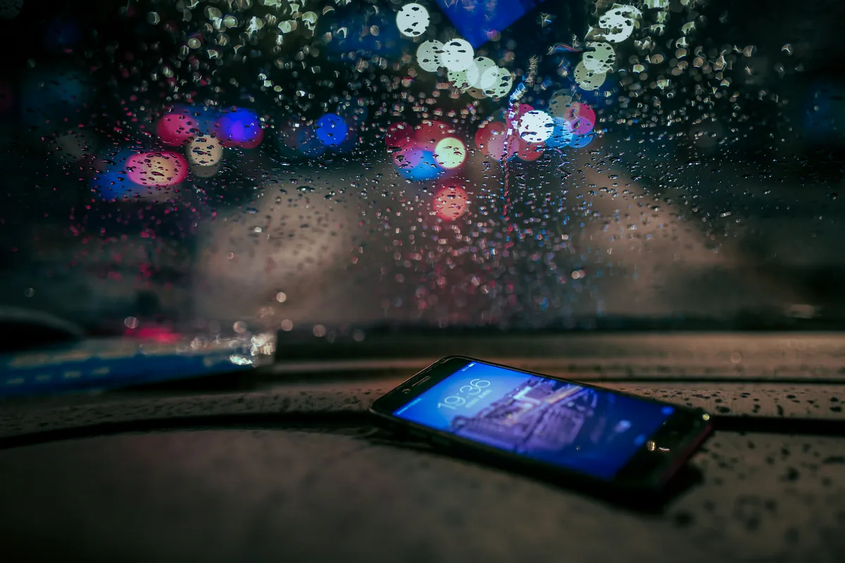 A phone lit up on a car dashboard on a rainy night